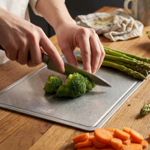 Chopping broccoli on a PureTi titanium cutting board with asparagus and carrots on a wooden bench