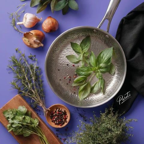 PureTi titanium hammered pan with fresh basil surrounded by herbs, garlic and onions on a purple background
