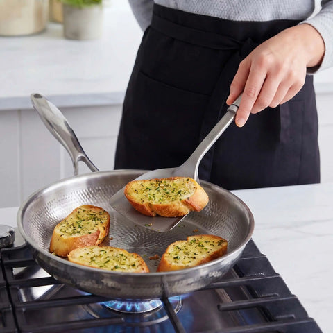 Cook in a black apron frying garlic bread in a PureTi titanium hammered pan with a titanium turner on a gas stove