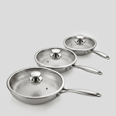 Three PureTi titanium hammered frying pans with glass lids on a light gray background