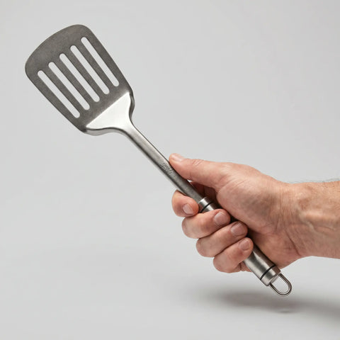 Hand holding a PureTi titanium slotted turner on a light gray background