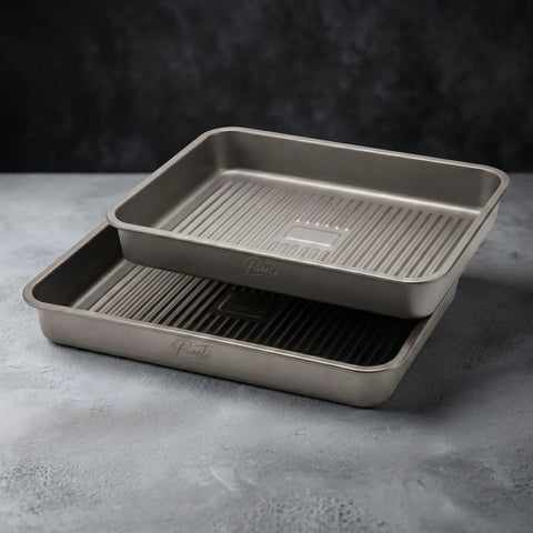 Two PureTi titanium baking trays stacked on a gray stone surface