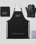 PureTi Signature Kitchen Set: black apron, silicone oven mitts, waffle weave towel and gift box on a light gray background
