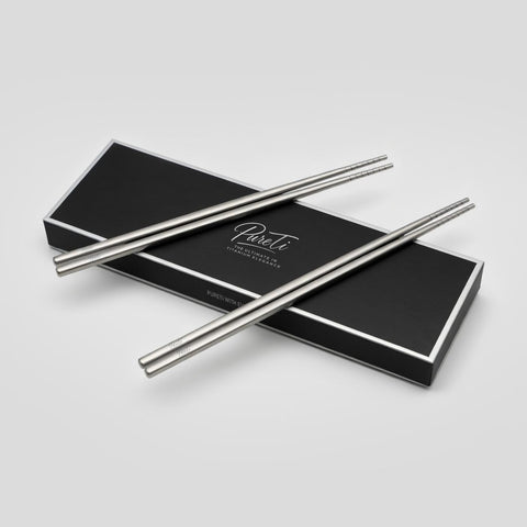 Pair of PureTi titanium chopsticks on a black box with 'PureTi' branding on a light gray background