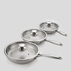 Three PureTi titanium hammered frying pans with glass lids on a light gray background