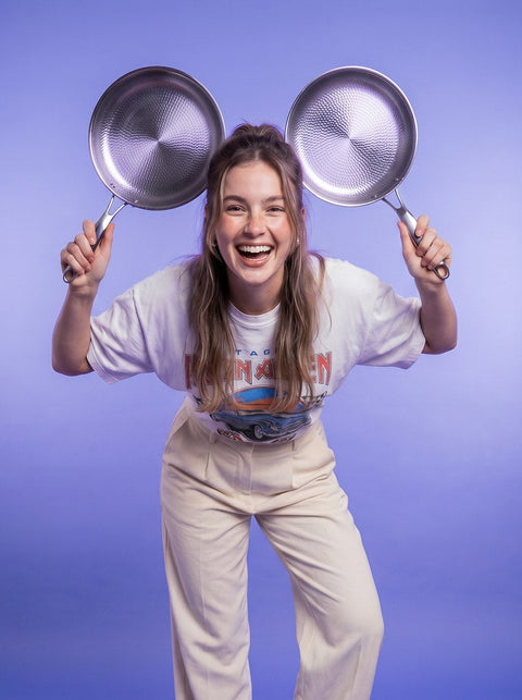Person holding two frying pans above their head against a purple background