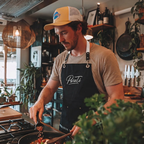 Man cooking in a kitchen wearing a 'Pureti' apron