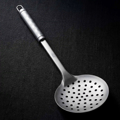 PureTi titanium slotted spoon on a black fabric background