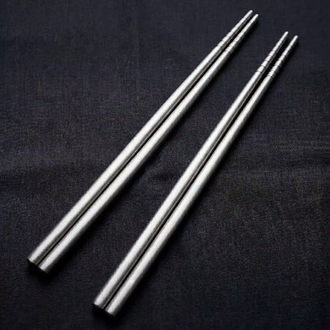 Two pairs of PureTi titanium chopsticks on a black fabric background