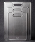 Three PureTi titanium cutting boards standing upright against a dark gray fabric background