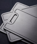 Close-up of three PureTi titanium cutting boards stacked on a black fabric background