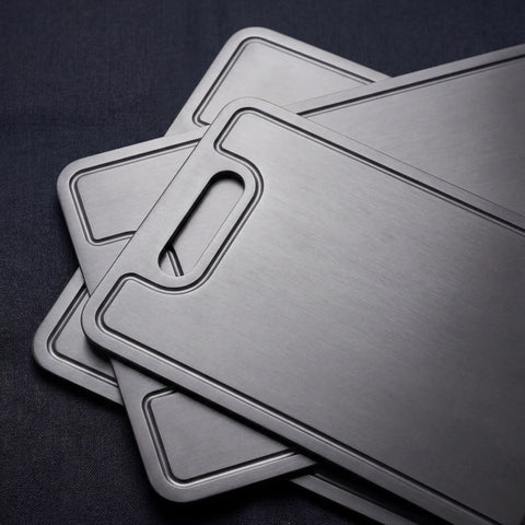 Close-up of three PureTi titanium cutting boards stacked on a black fabric background
