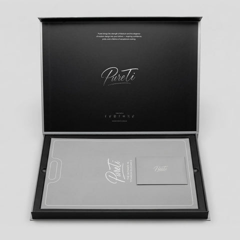 Open black box and gray sleeve for the PureTi titanium cutting board with 'PureTi' branding on a light gray background