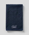 Folded navy PureTi waffle weave cotton kitchen towel with embroidered logo on a light gray background