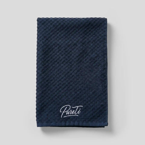 Folded navy PureTi waffle weave cotton kitchen towel with embroidered logo on a light gray background
