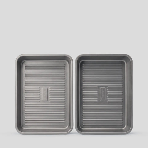 Two PureTi titanium baking trays with ridged bases, top view on a light gray background